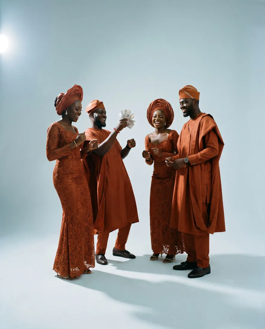 Four friends in the same burnt-orange aso ebi lace, gèlè and agbada, laughing and spraying money